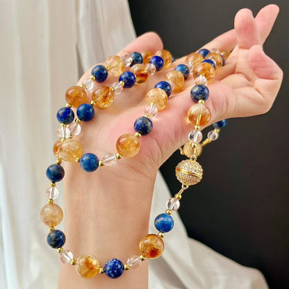 Hand holding lapis and citrine necklace against curtain light
